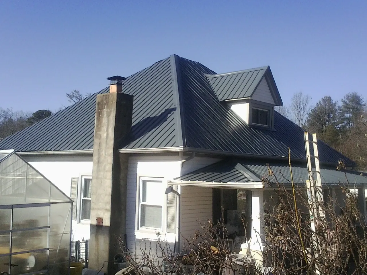 Dark blue standing seam metal roof on a white farmhouse with dormer — Slate & Tile Roof Repair by Roofing Brothers in Harbor View