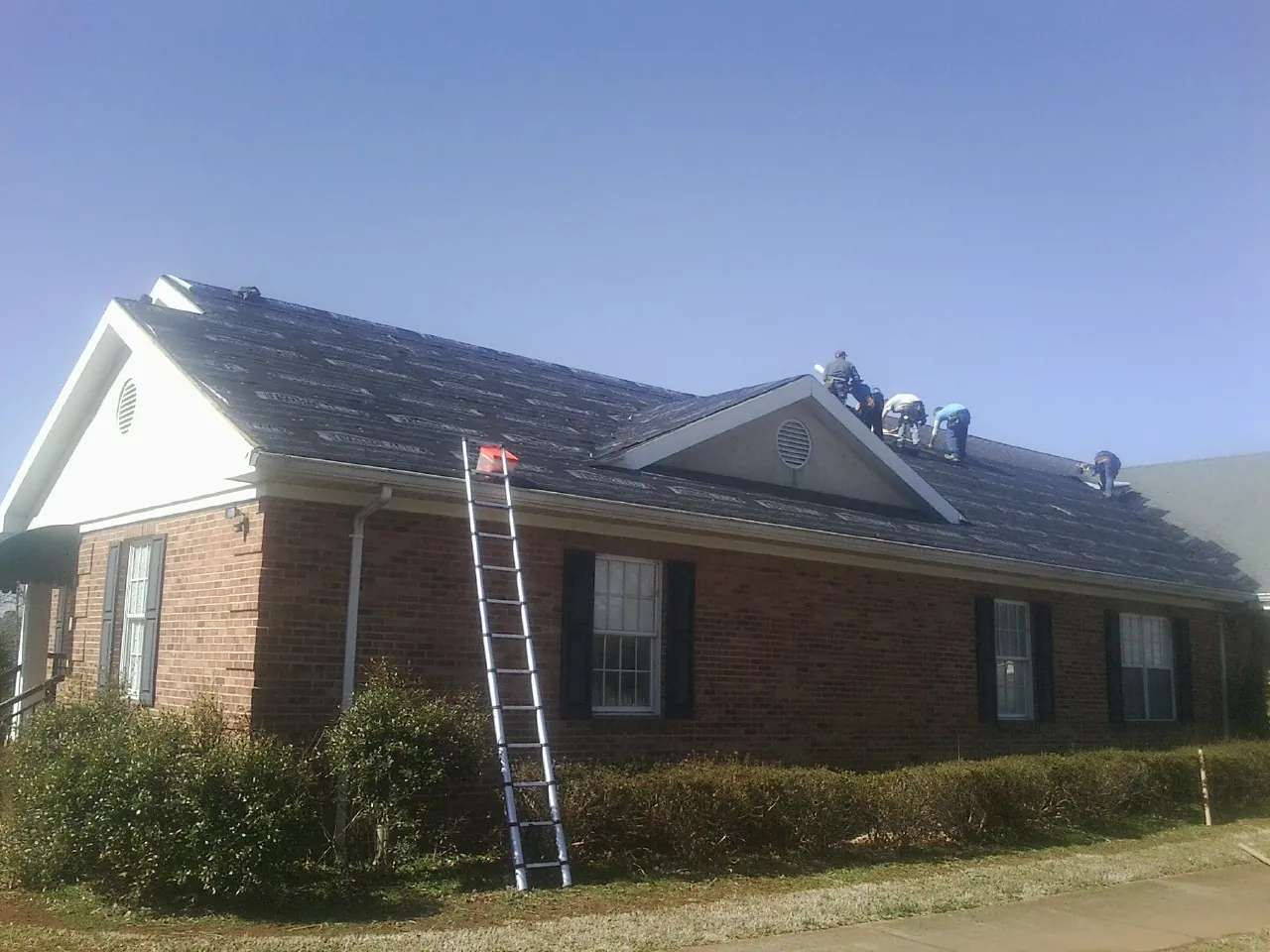 Crew tearing shingles off a brick ranch roof with a ladder set — Emergency Roof Repair work by our crew in Harbor View