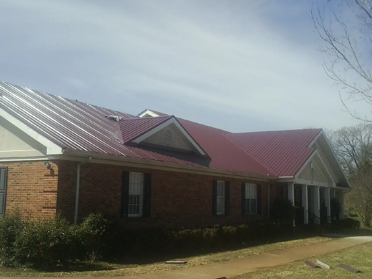 Red metal roof with gabled entries on a long brick building, from a Hail Damage Roof Repair job in Harbor View