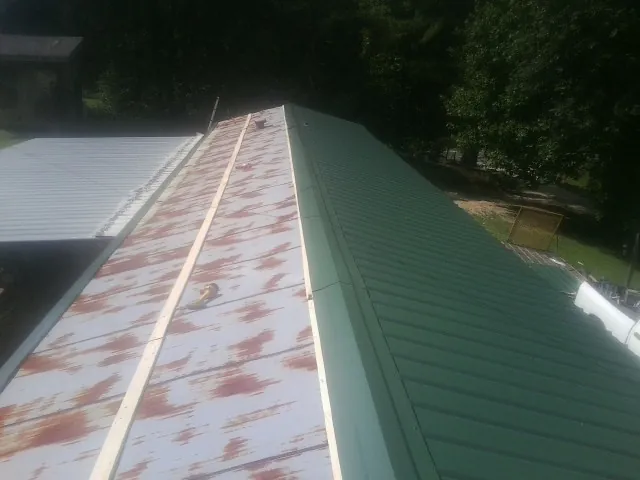 Old rusted panels beside newly installed green metal roofing — Wind Damage Roof Repair by Roofing Brothers in Harbor View