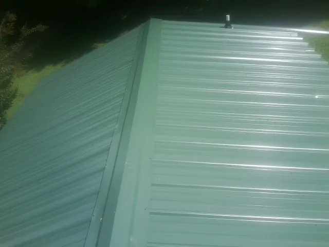 New green metal panels meeting at the ridge of a roof — Flat Roof Repair work by our crew in Harbor View