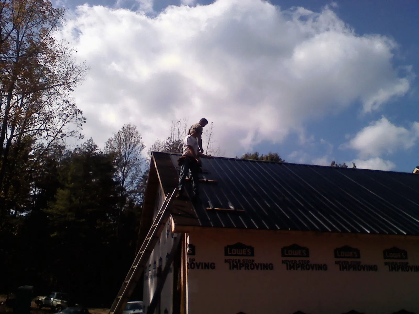 Roofer fastening dark metal panels high against a cloudy sky, from a Roof Inspection job in Harbor View