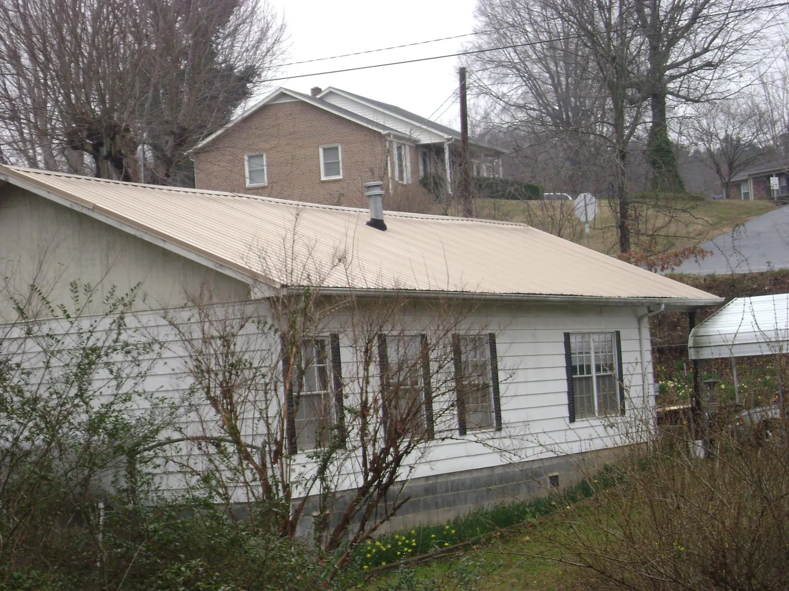 Tan metal roof on a white sided house set into a hillside — Commercial Roofing by Roofing Brothers in Harbor View